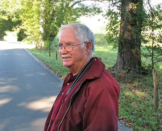 A man wearing glasses and a red jacket stands on the side of a road