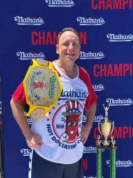 Joey Chestnut, winner of the Nathan's Hot Dog Eating Contest, holding a championship belt and trophy.