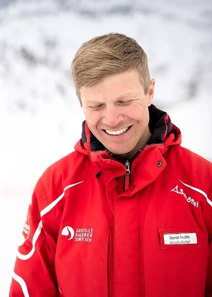 Skischulleiter Daniel lächelt frontal in die Kamera und blickt dabei nach unten
