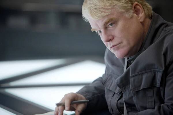 Person sitting at a lit table, holding a pen, appearing pensive. Wearing a casual jacket, interacting with an unseen object or document