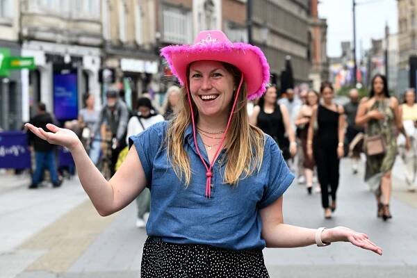 Woman in pink cowboy hat on city street.