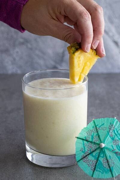Woman adding a slice of pineapple to a pina colada.