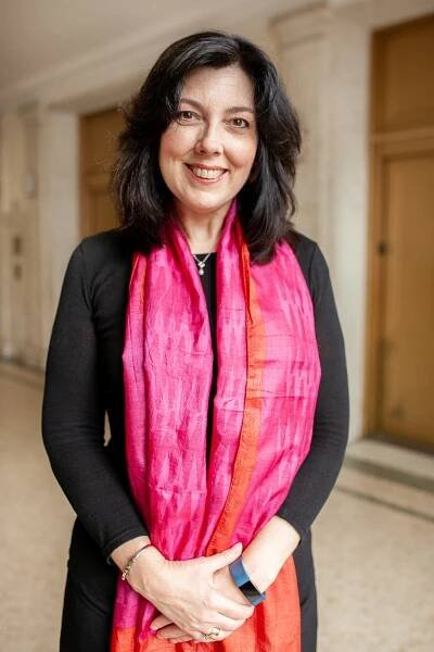 A woman in a black dress with a fuchsia scarf smiles in a portrait.