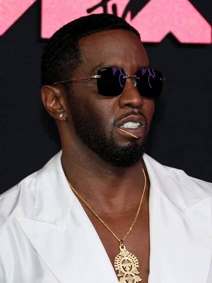Sean Combs, in a white jacket, gold chain and sunglasses, poses with a toothpick in his mouth.