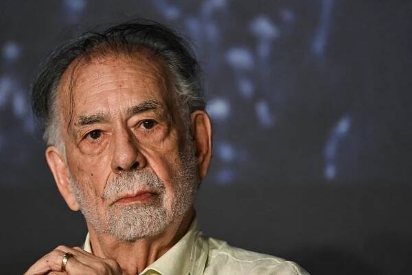 Francis Ford Coppola, in a light-colored collared shirt, looks serious as he clasps his hands near his chin.