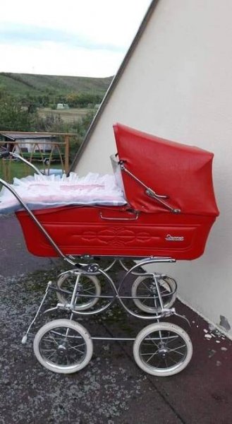 a red baby stroller sitting next to a building