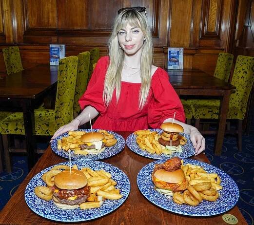 Woman in red dress at a table with four gourmet burgers and fries.