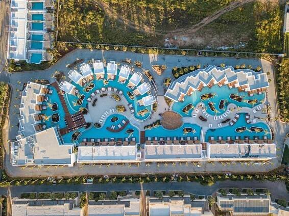 Stella Island Luxury Resort & Spa (Adults Only) Hersonissos  Exterior photo The photo shows an aerial view of a resort complex, likely located in a warm, sunny climate. The resort features several low-rise buildings with white facades and distinctive, curved rooflines, giving it a modern and somewhat whimsical appearance. 

