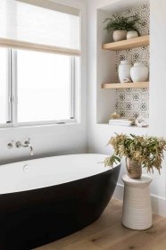 A bathroom with a black bathtub and several wooden shelves backed by printed wallpaper