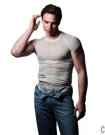 a man in a fitted tshirt and unzipped jeans striking a thoughtful pose