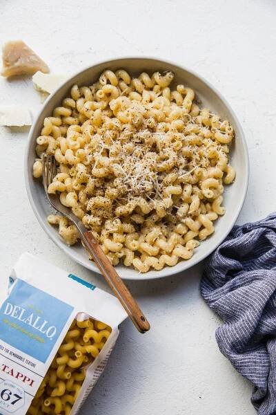 homemade Creamy Cavatappi  in a bowl with a fork next to a linen napkin and a bag of DeLallo Cavatappi pasta