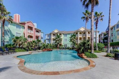 a swimming pool with palm trees and condos at The Dawn Condominiums in Galveston