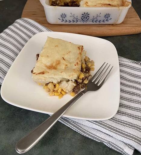 Shepherd's pie on a white plate with a fork on top of a dish cloth.