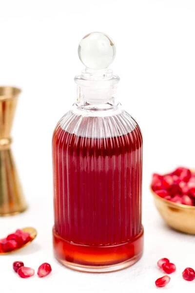 A glass bottle filled with red liquid, accompanied by pomegranate seeds and a brass container.