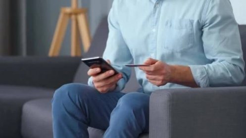 Formálně oblečený muž sedí na gauči a zadává číslo kreditní karty do smartphonu, aby zaplatil online. Online nakupování, technologie životního stylu — Stock záběr