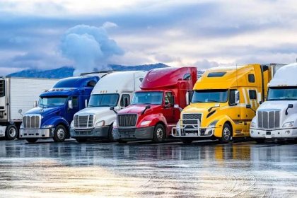 jasně barevné velké soupravy náklaďáky s návěsy stojící v řadě na parkovišti pro kamiony brzy ráno - ground transportation - stock snímky, obrázky a fotky