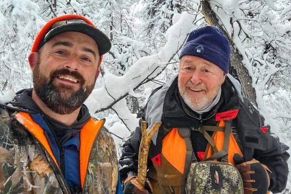 Two men wearing camo and blaze orange hunting in the fresh snow