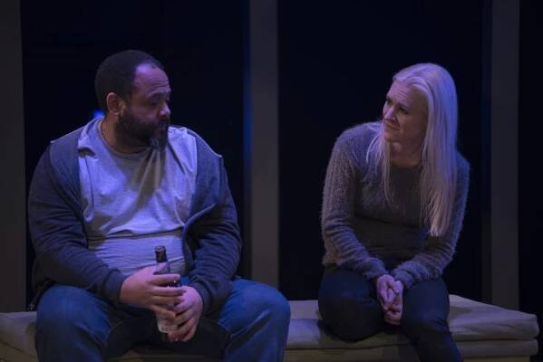 a man and a woman with a bottle of alcohol sit on a bench talking