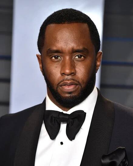 A man in a beard and a black tuxedo poses, solemnly.