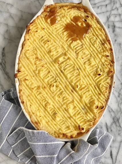 Golden mashed potato-topped turkey shepherd's pie in a white oval dish on a striped cloth.