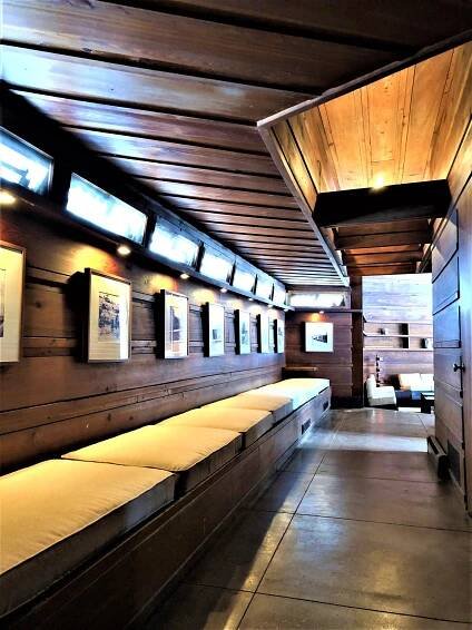 A long hallway has a storage bench with cushions on top and historic photos on the walls.