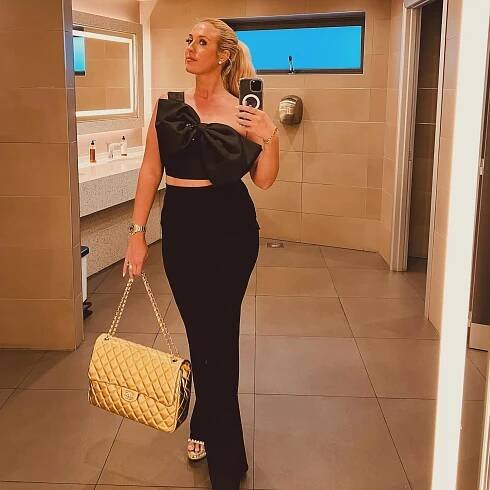 Woman in black outfit taking a selfie in a bathroom.