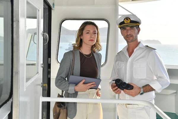 „Das Traumschiff: Argentinien“: An Deck des Schiffs: Cora Bruns (Friederike Linke steht neben Kapitän Parger (Florian Silbereisen). Beide blicken fokussiert in die Ferne. Cora Bruns hält ein Tablet in der Hand, Kapitän Parger ein Fernglas.