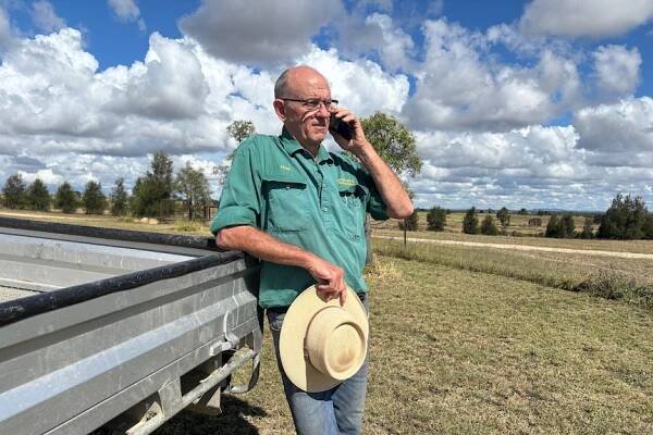 Peter Thompson leans against a ute on mobile phone.