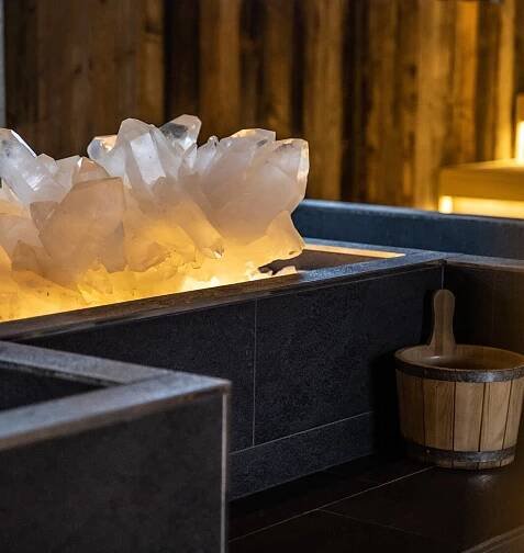 Detailaufnahme Bergkristall in dunklem Becken neben Holzeimer im Saunabereich