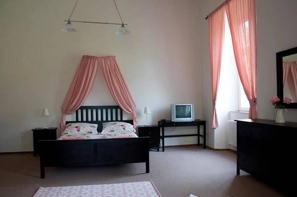 a bedroom with a bed with pink curtains and a television at Penzion Zámek Rozsochatec in Rozsochatec