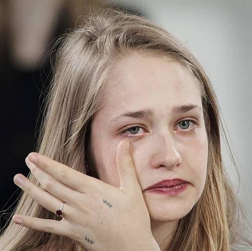 a woman with long blonde hair holding her hand up to her face and looking at the camera