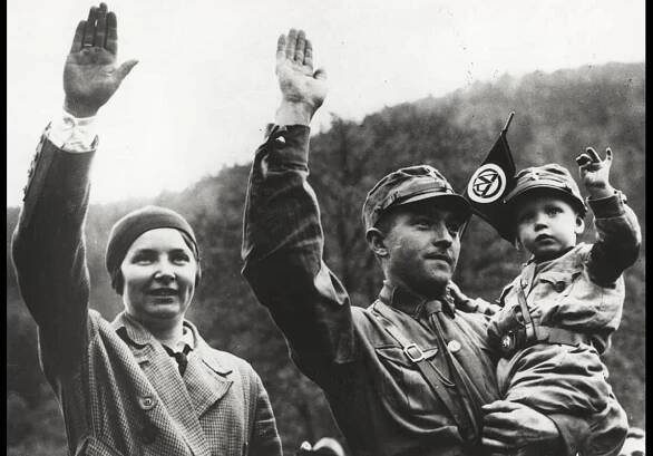 A SA member and his son performing a ‘Heil Hitler’ salute. Both are wearing the traditional brown SA uniform. 