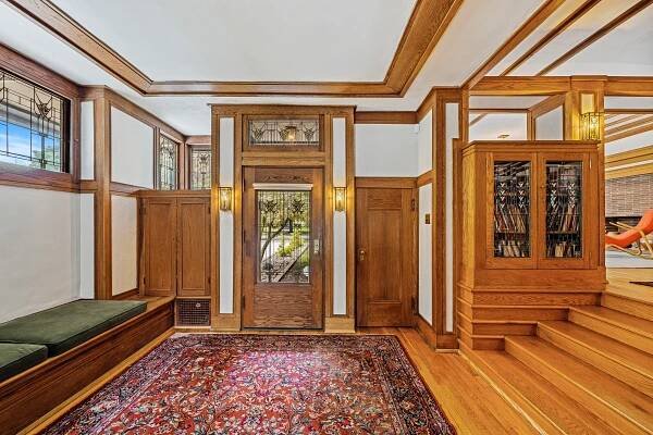 Interior view of a Frank Lloyd Wright prairie home's entryway, featuring wood paneling, stained-glass windows, and a built-in bookcase.