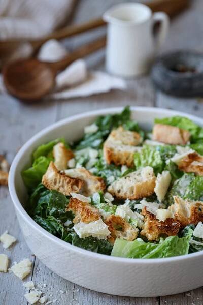 a salad in a white bowl with croutons and parmesan cheese