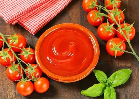 Tomato passata in orange dish next to vine ripened tomatoes and red checkered kitchen towel.