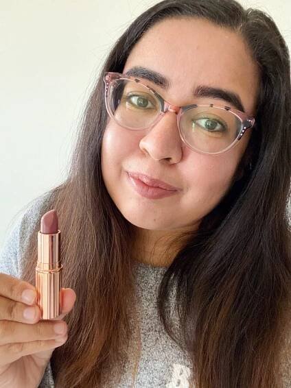 A woman holding Charlotte Tillbury lipstick swatched on her lips 