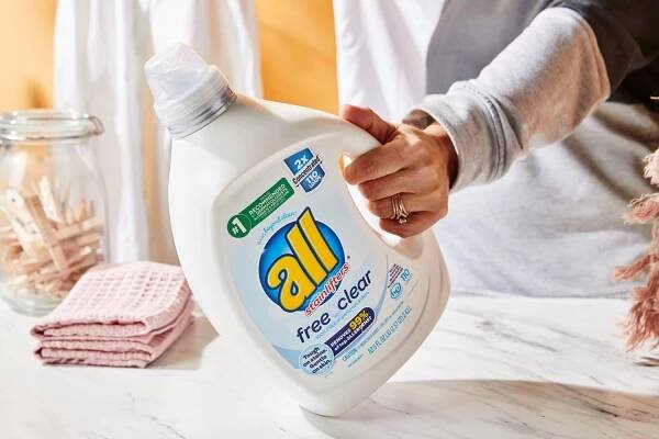 Hand holding All Free Clear Liquid 2x Concentrated Laundry Detergent on marble countertop
