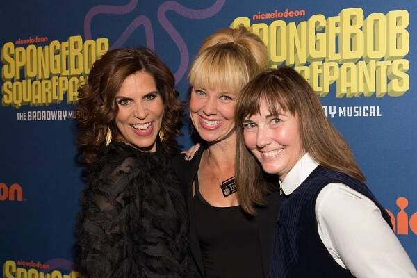 Three women smiling at a "SpongeBob SquarePants: The Broadway Musical" event backdrop