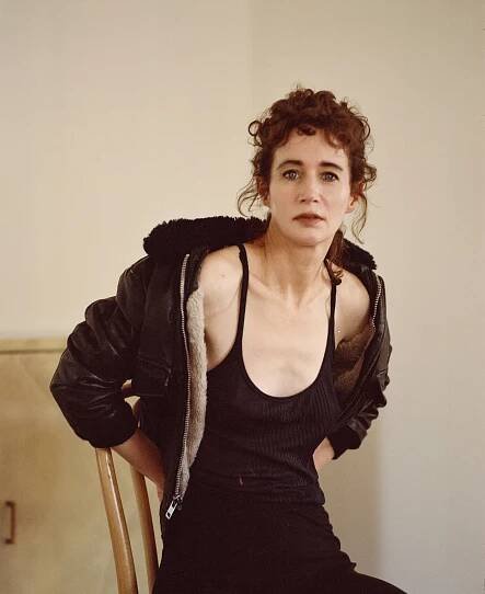 Sitting on a chair, Ms. July wears a black spaghetti-strap tank top underneath a leather jacket with fleece trim.
