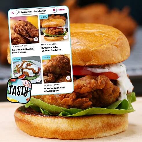 Close-up of a gourmet fried chicken sandwich with lettuce and tomatoes, overlaid with a smartphone screen showing various fried chicken recipe options