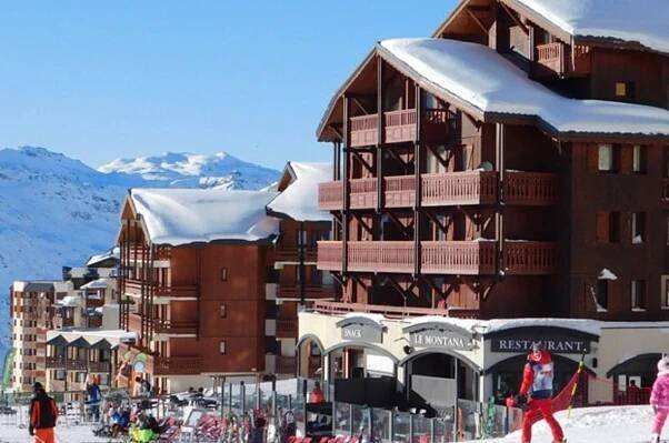 A group of people skiing in front of a building that says restaurant