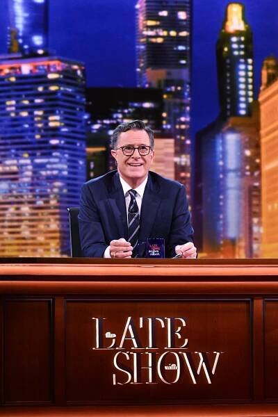 Stephen Colbert in a suit behind a desk.