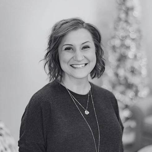 A woman wearing a black sweater and a necklace is smiling in a black and white photo.