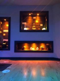 a yoga room with a purple wall containing lit up shelves of buddhist statues