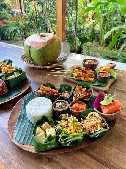 a wooden table topped with lots of food on top of green leafy plates and bowls