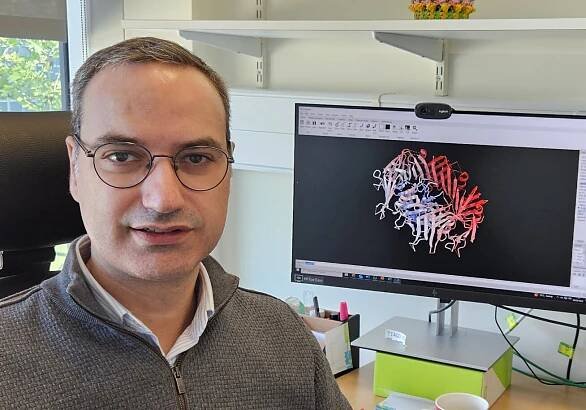Tiago in his office with a computer graphic of a protein in the background