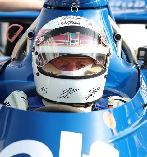 Auto racing helmet with signatures and tartan design resting on a blue race car.