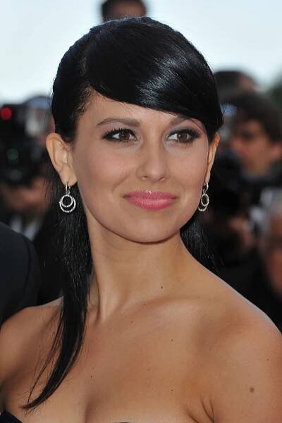 Person with sleek hairstyle and hoop earrings on a red carpet, wearing a strapless dress