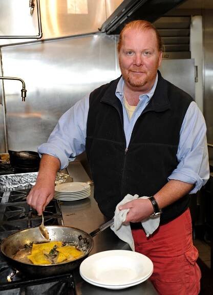 Mario Batali wearing a fleece navy vest in the kitchen cooking ravioli. 