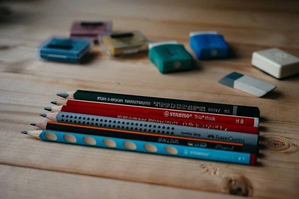several pencils are lined up on a wooden table with erasers and sharpeners